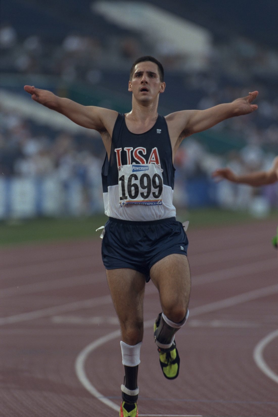 Tony Volpentest crossing the finish line in a USA singlet, arms outstretched